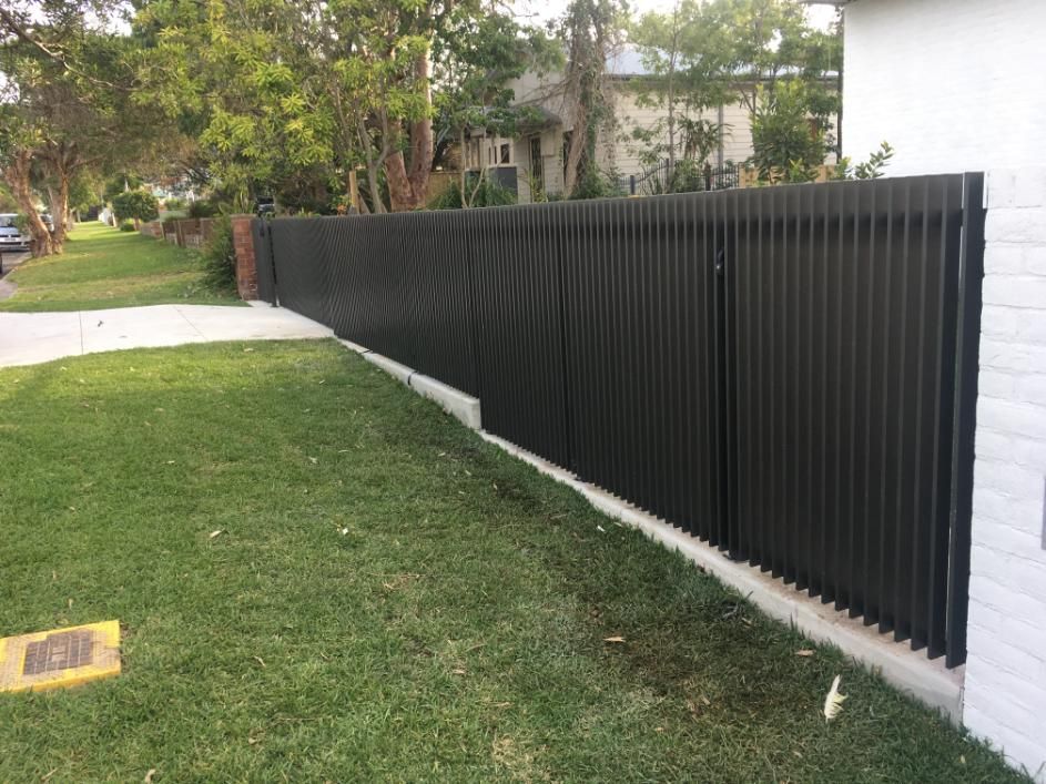 A Black Fence Surrounds a Lush Green Yard in Front of a White House — Lifestyle Aluminium Fabrication In Dapto, NSW