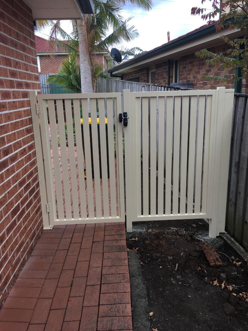 A White Gate is Sitting Next to a Brick Wall — Lifestyle Aluminium Fabrication In Fairy Meadow, NSW