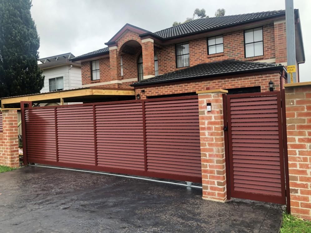 A Large Brick House With a Red Sliding Gate in Front of It — Lifestyle Aluminium Fabrication In Fairy Meadow, NSW