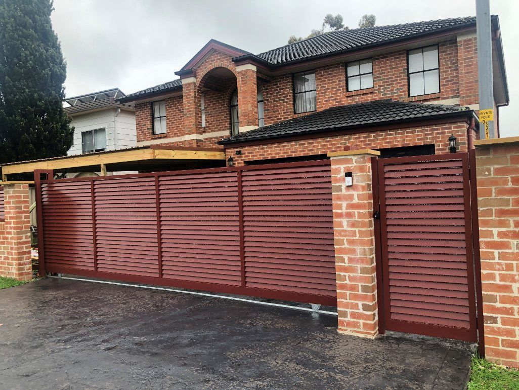 A Large Brick House with A Red Gate in Front of It — Lifestyle Aluminium Fabrication In Albion Park Rail, NSW
