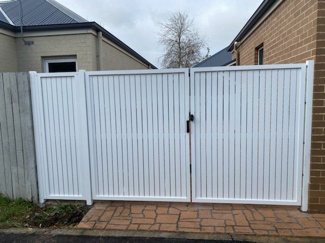 A White Gate Is Sitting in Front of A Brick House — Lifestyle Aluminium Fabrication In Albion Park Rail, NSW