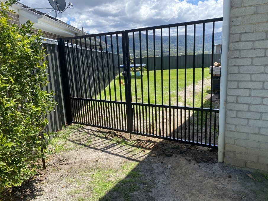 A Black Gate Is Sitting in Front of A White Brick Building — Lifestyle Aluminium Fabrication In Albion Park Rail, NSW