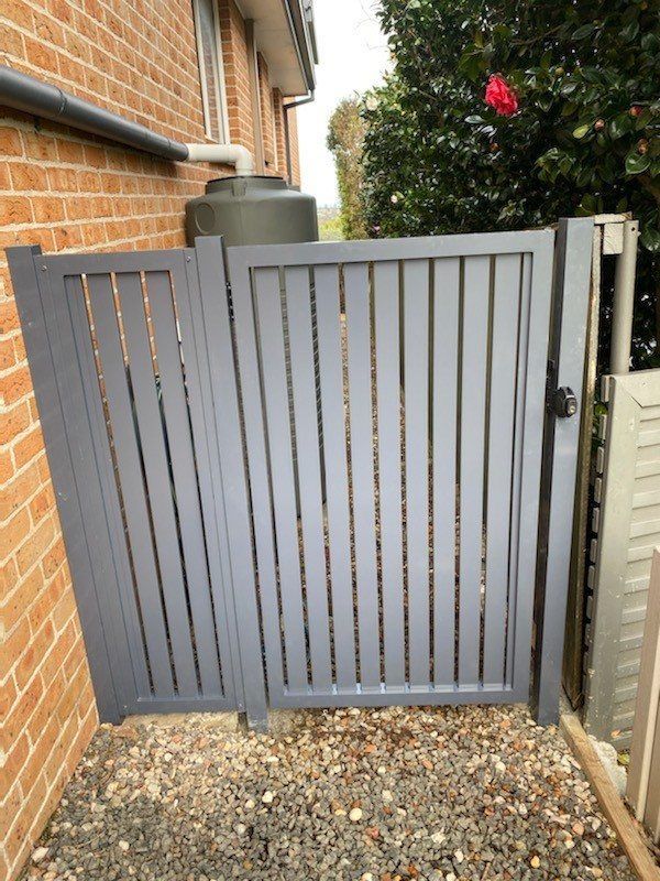 A Gray Gate Is Sitting Next to A Brick Building — Lifestyle Aluminium Fabrication In Albion Park Rail, NSW