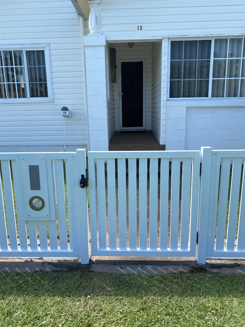 A White Fence Surrounds a White House with A Black Door — Lifestyle Aluminium Fabrication In Albion Park Rail, NSW