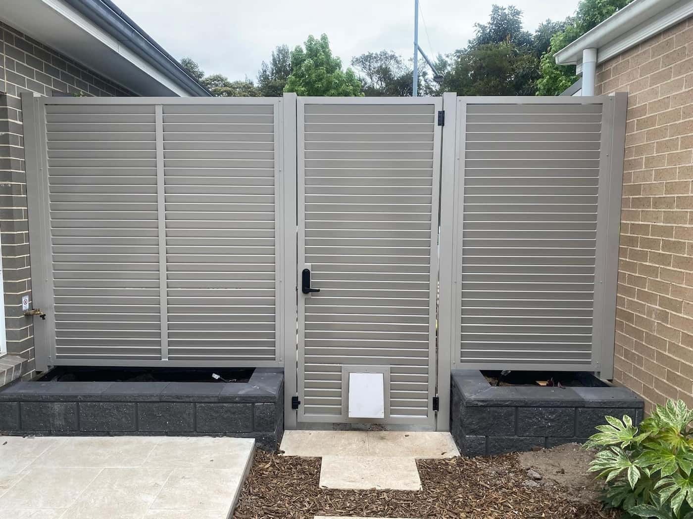 A Stainless Steel Gate Is Sitting in Front of A Brick Building — Lifestyle Aluminium Fabrication In Kiama, NSW