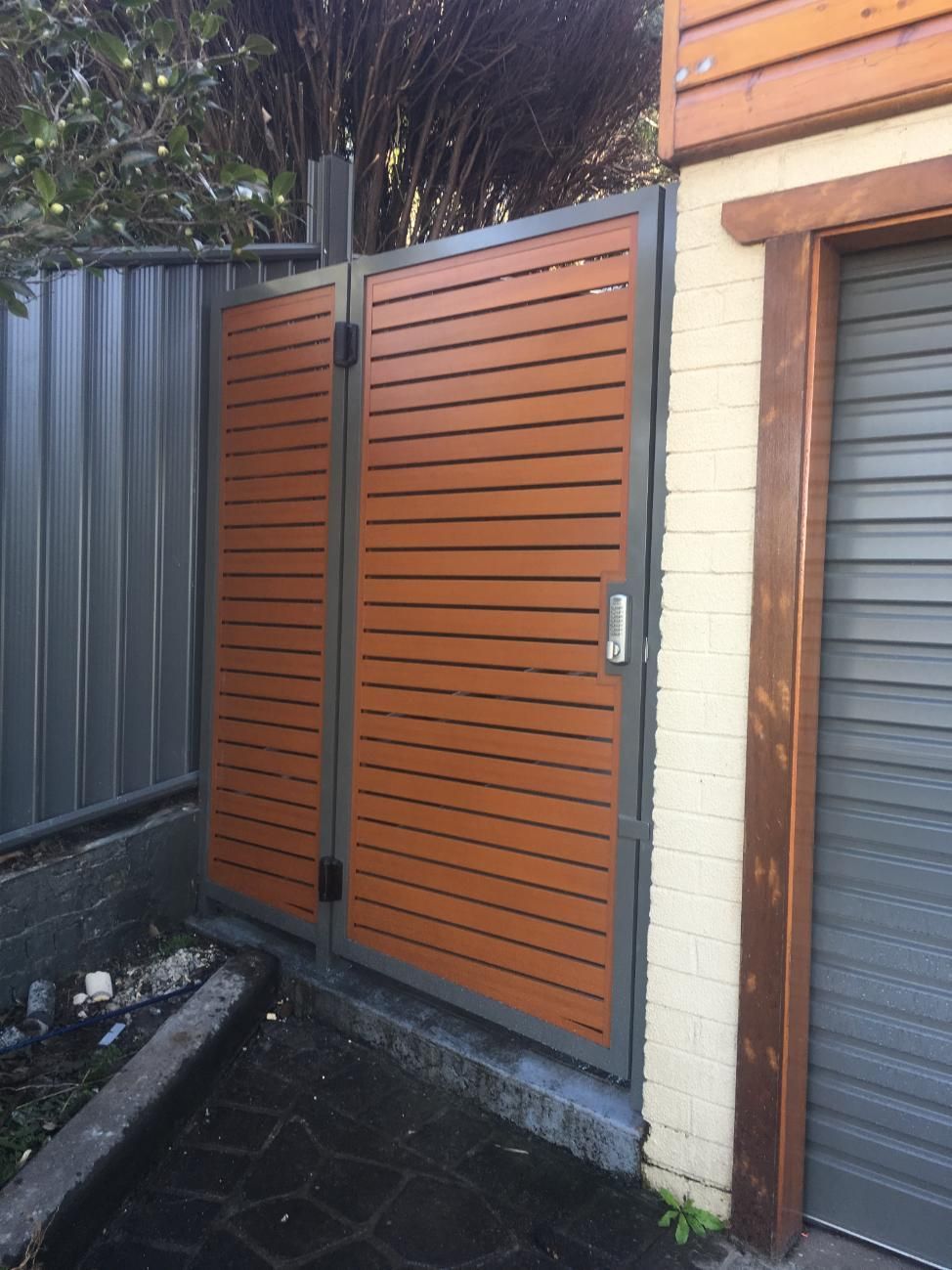 A Wooden Gate is Sitting Next to a Garage Door — Lifestyle Aluminium Fabrication In Shellharbour, NSW
