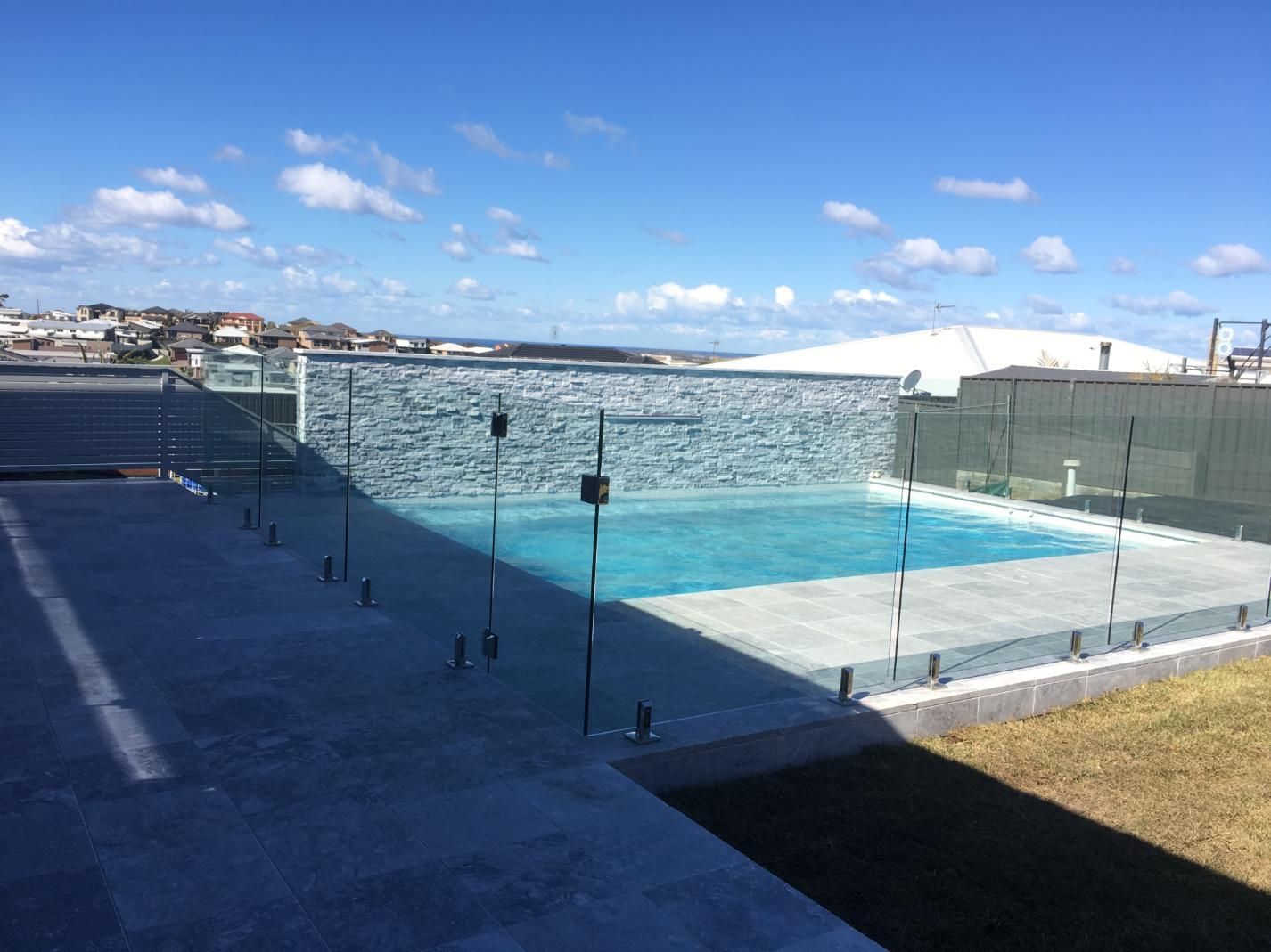A Large Swimming Pool With a Glass Fence Around It — Lifestyle Aluminium Fabrication In Fairy Meadow, NSW