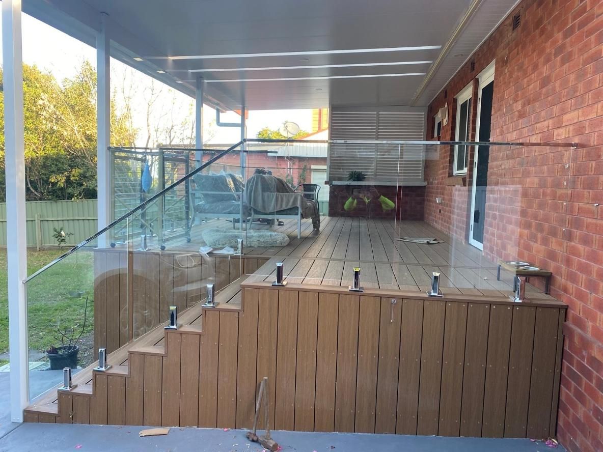 A Brick House With a Deck and Stairs With a Glass Railing — Lifestyle Aluminium Fabrication In Wollongong, NSW