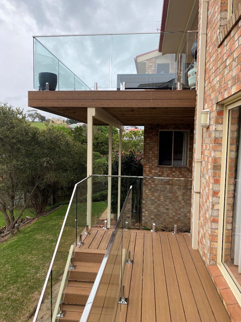 A Dog Is Sitting on A Porch with A Glass Railing — Lifestyle Aluminium Fabrication In Albion Park Rail, NSW