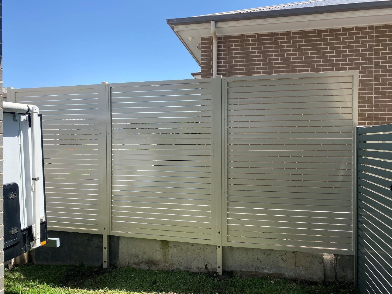 A White Van Is Parked Next to A Fence in Front of A Brick Building — Lifestyle Aluminium Fabrication In Albion Park Rail, NSW