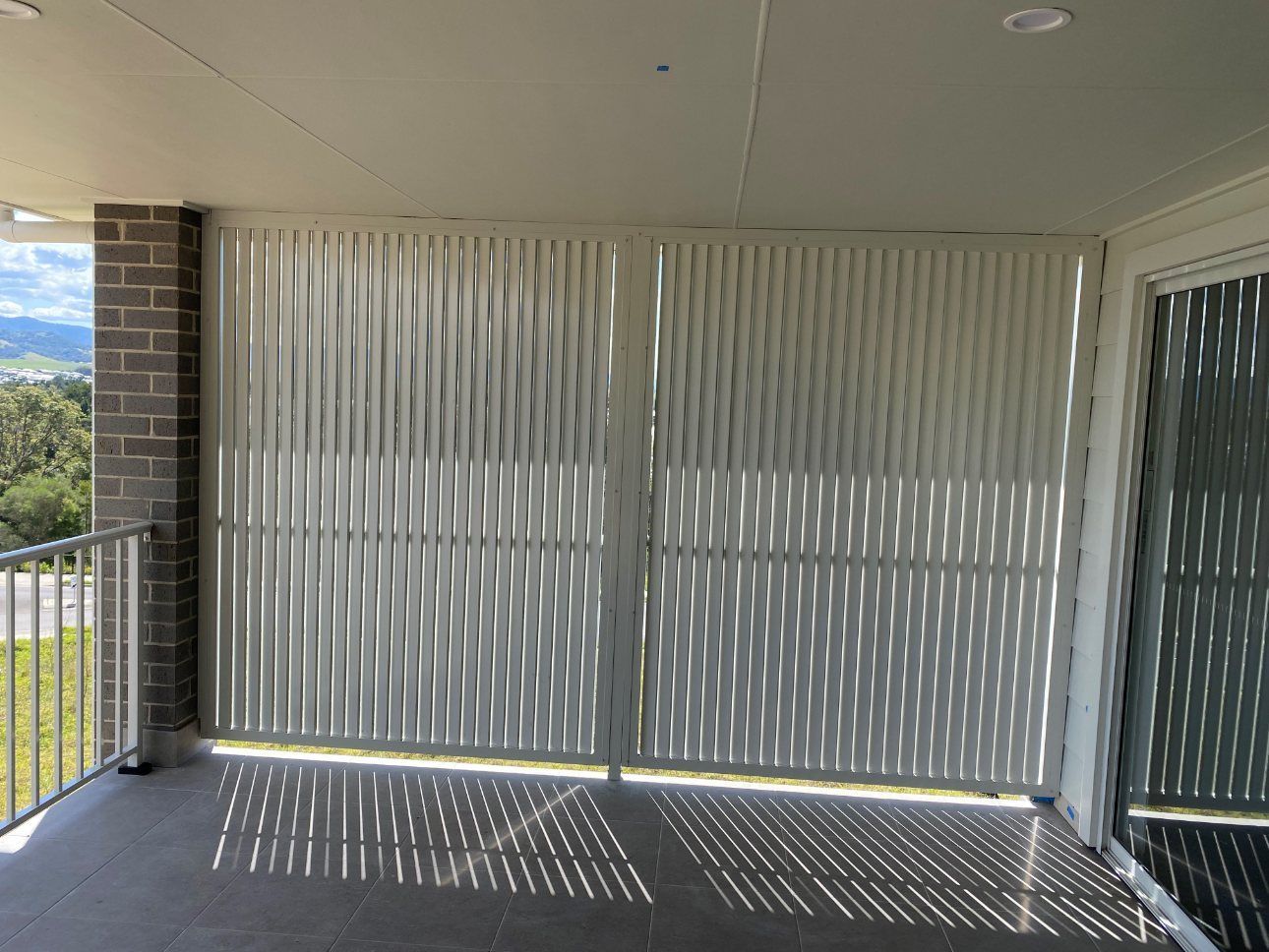 A Balcony with A White Fence and Sliding Glass Doors — Lifestyle Aluminium Fabrication In Albion Park Rail, NSW