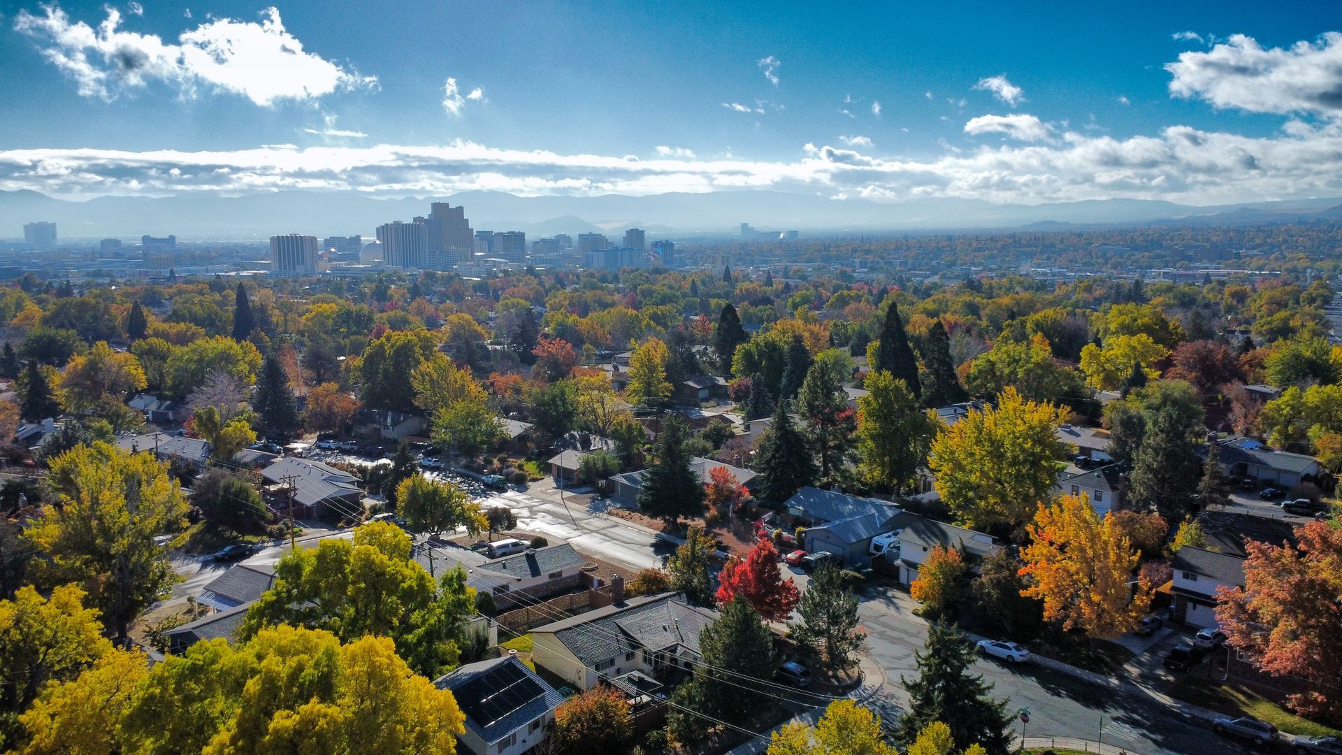 Aerial view of a city with fall foliage, buildings in the distance, and blue sky.