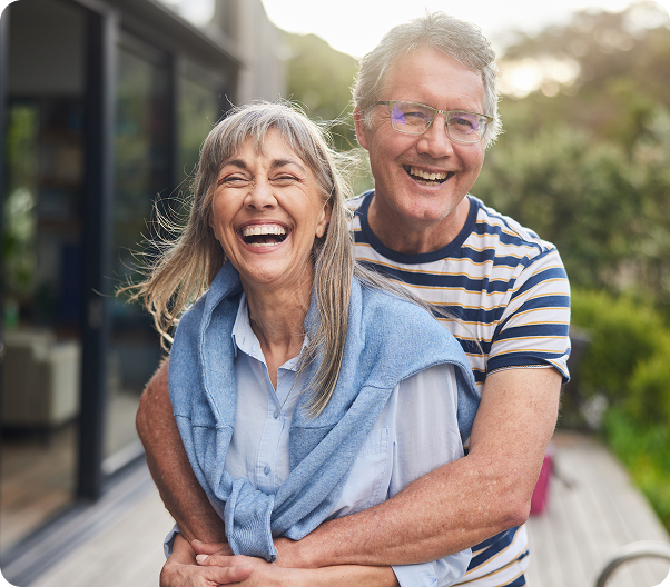 Smiling older couple embracing on a deck; woman with gray hair, man in striped shirt.