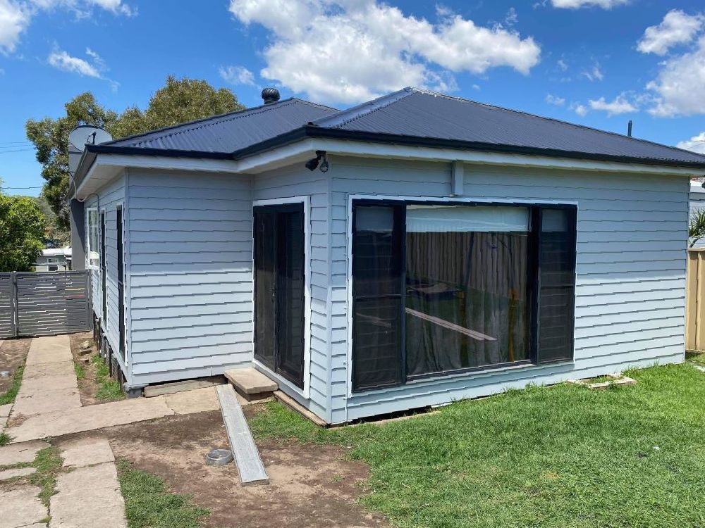 A White House With A Black Roof Is Sitting On Top Of A Lush Green Field — In-Time Roofing In Newcastle, NSW