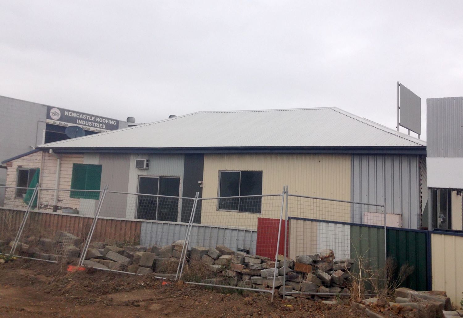 A House With A White Roof Is Surrounded By A Fence And Rocks — In-Time Roofing In Newcastle, NSW