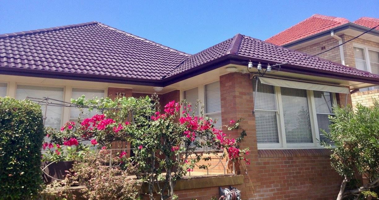 A Brick House With A Tiled Roof And Flowers In Front Of It — In-Time Roofing In Newcastle, NSW