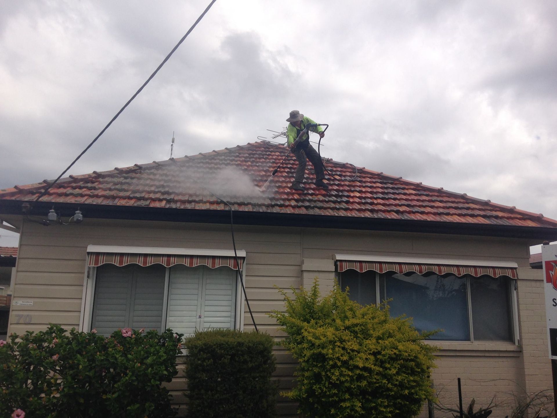 A Man Is Cleaning The Roof Of A House With A High Pressure Washer — In-Time Roofing In Newcastle, NSW