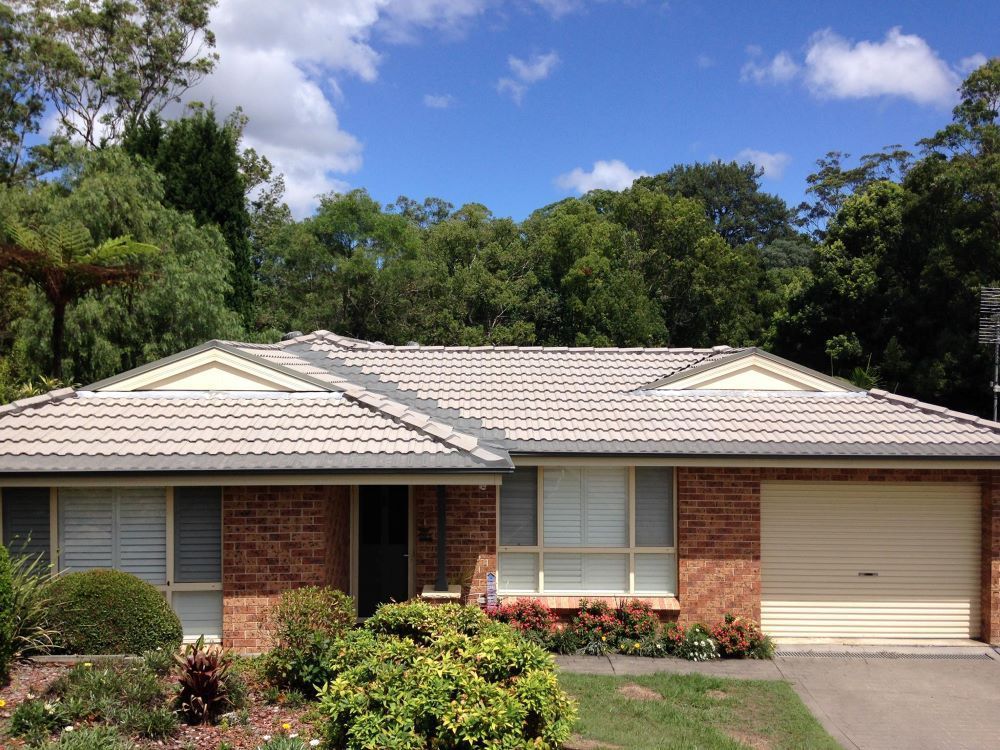 A Brick House With A Tiled Roof And A White Garage Door — In-Time Roofing In Newcastle, NSW