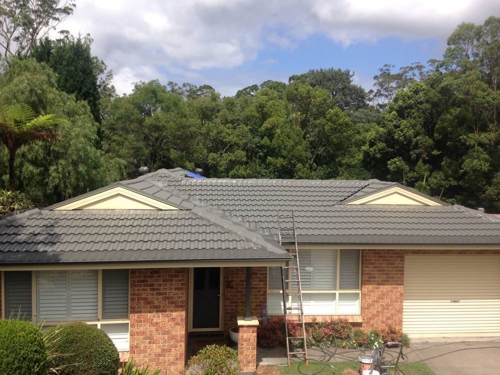 A Brick House With A Gray Roof And A White Garage Door — In-Time Roofing In Newcastle, NSW