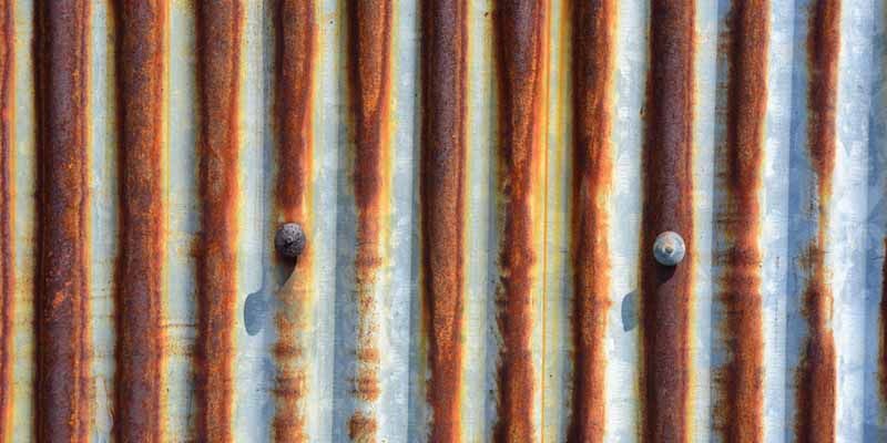 A Close Up Of A Rusty Corrugated Metal Wall With Nails — In-Time Roofing In Newcastle, NSW