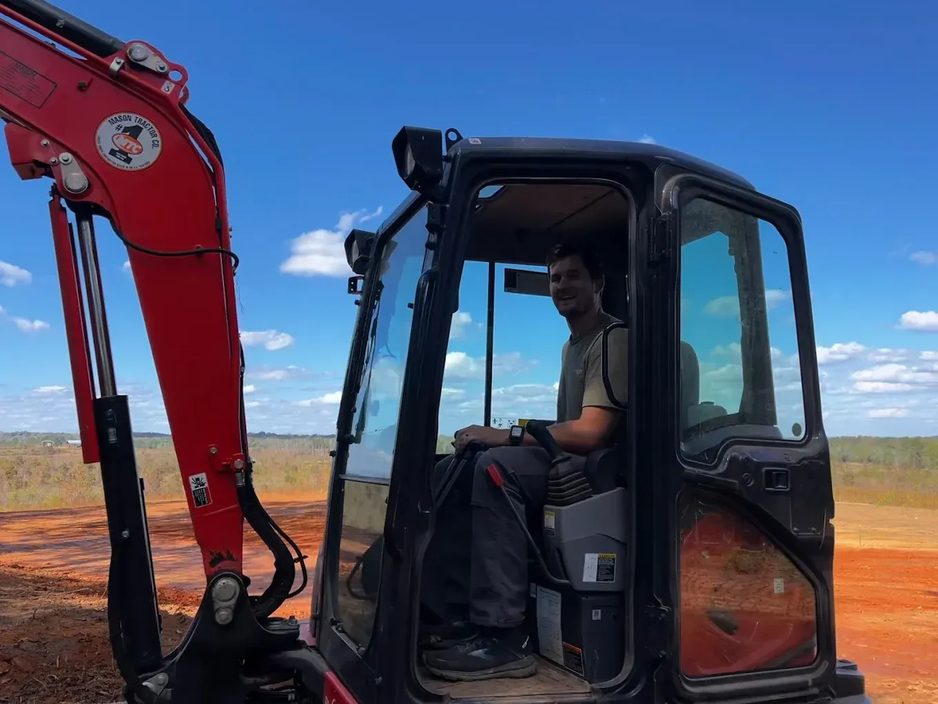 Woman in straw hat smiles, holding wine glass near a lake.