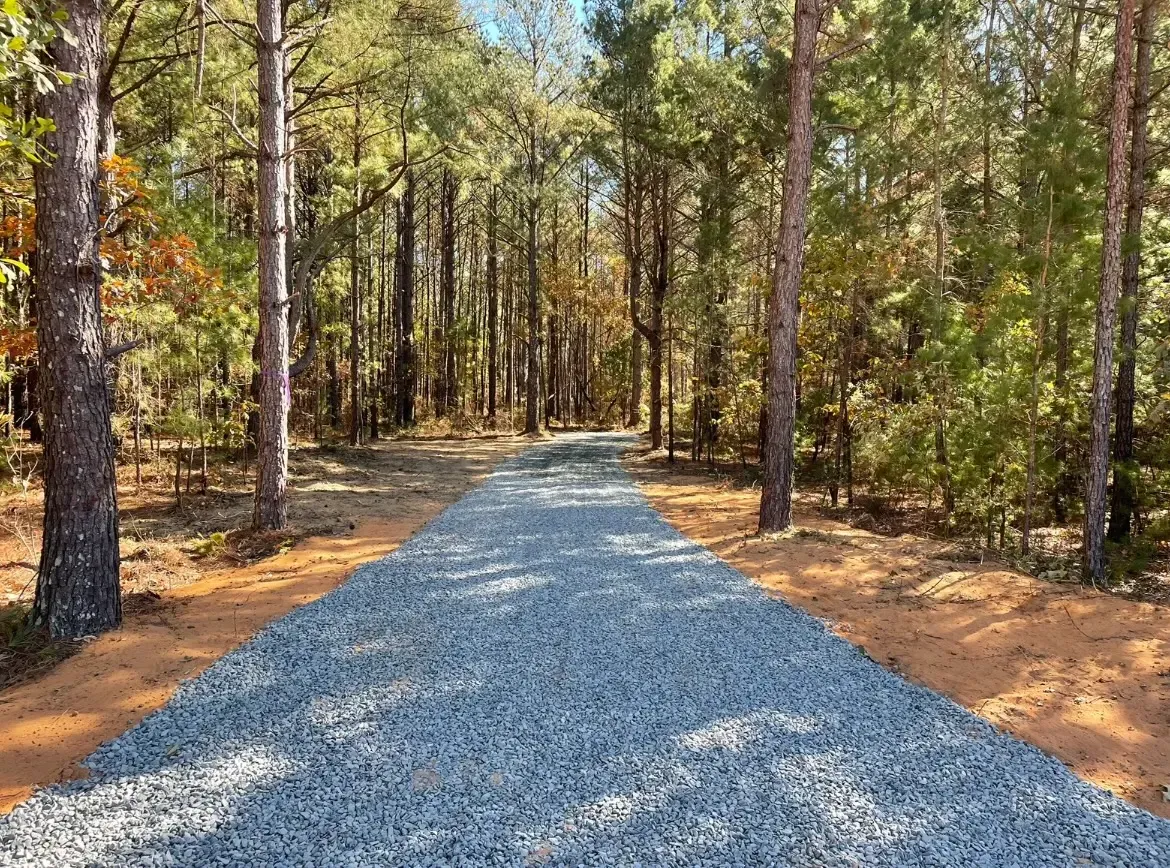 Woman in straw hat smiles, holding wine glass near a lake.