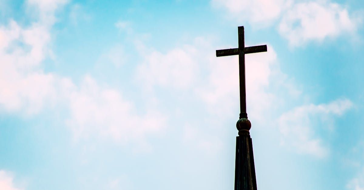 A church steeple with a cross on top of it against a cloudy blue sky.