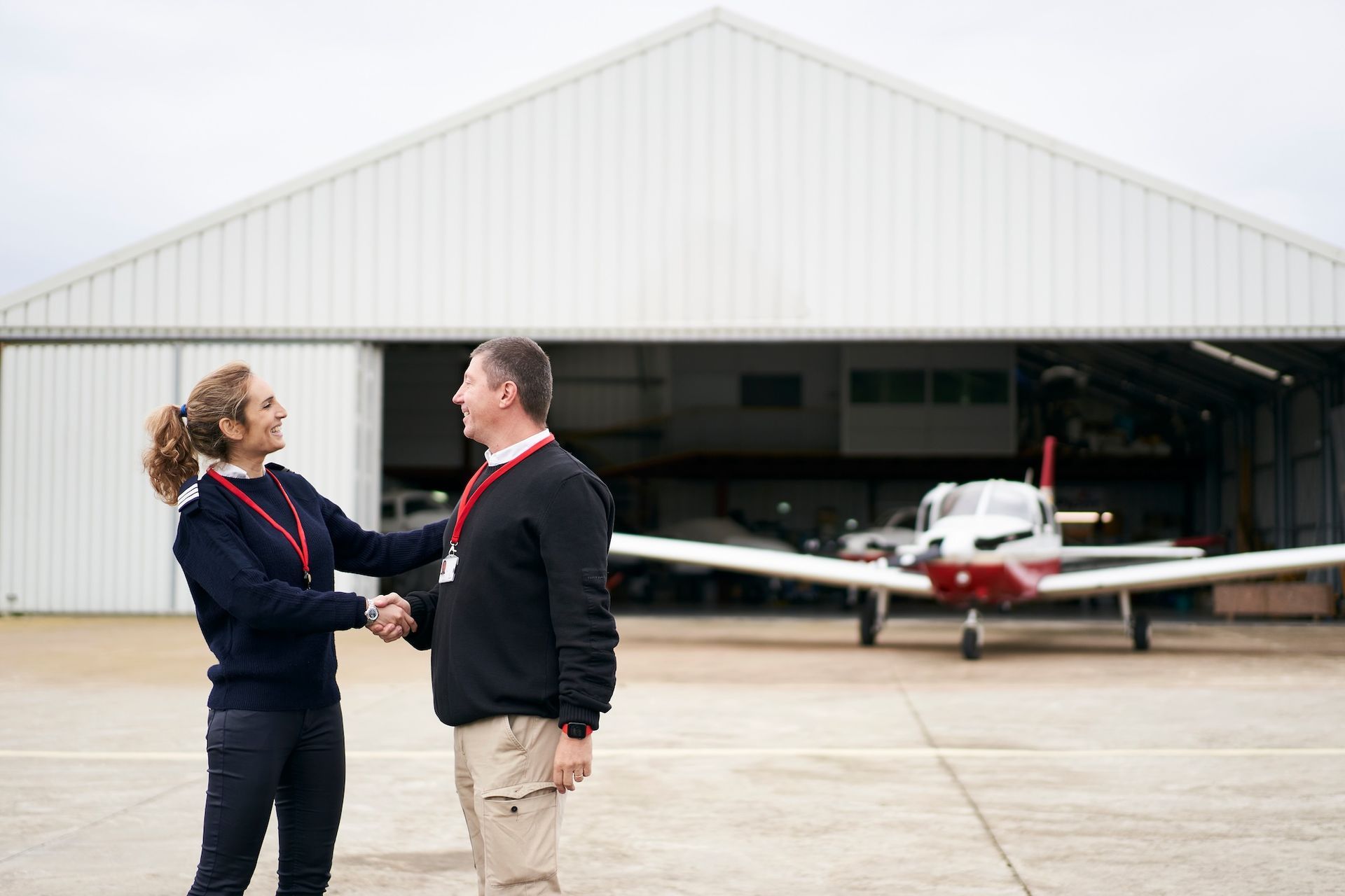 Flight instructor congratulating a student pilot outside an aircraft hangar after earning a license.