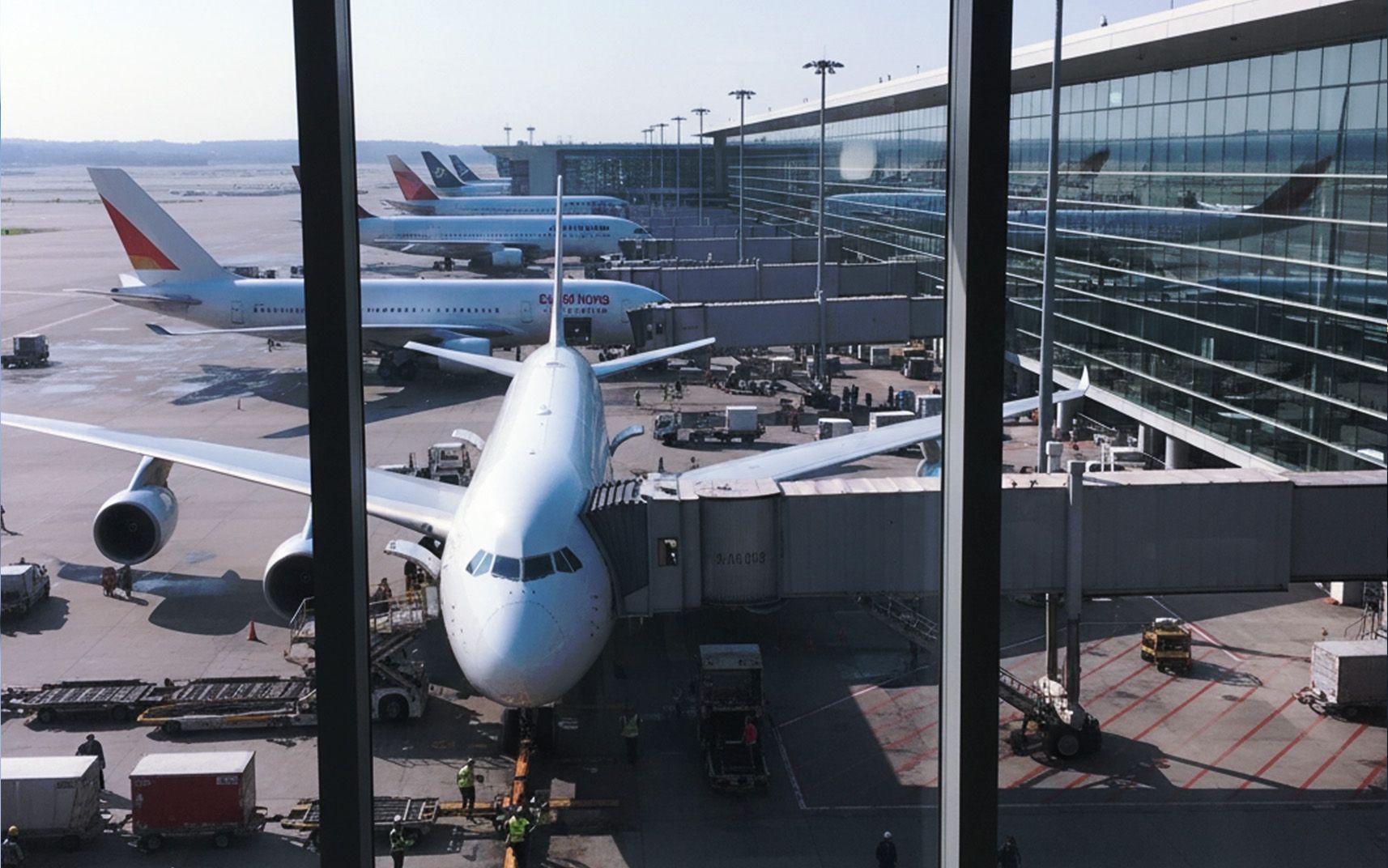 Commercial airliner parked at airport gate seen through terminal window.