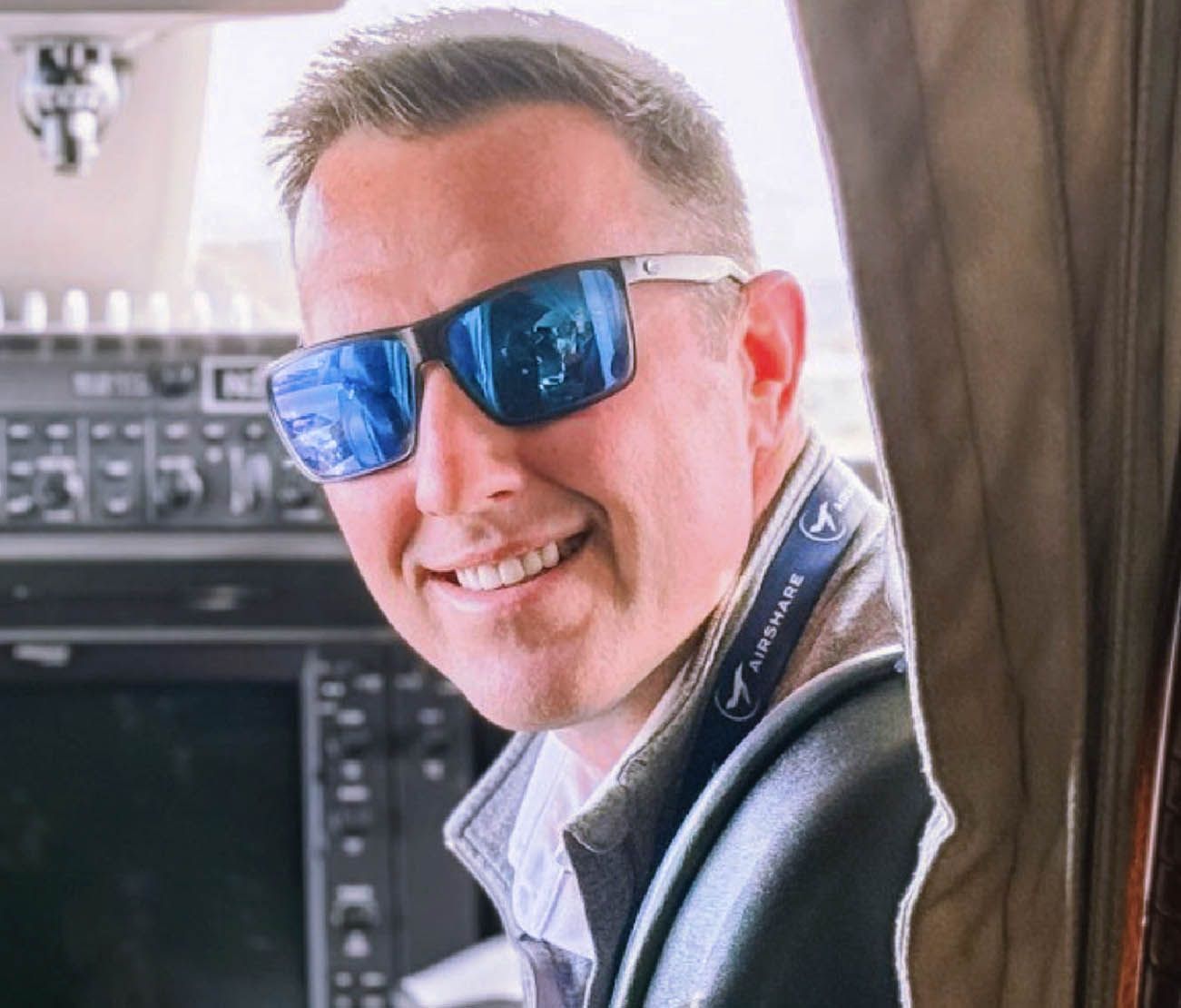 Pilot in sunglasses sitting in cockpit for testimonial photo.
