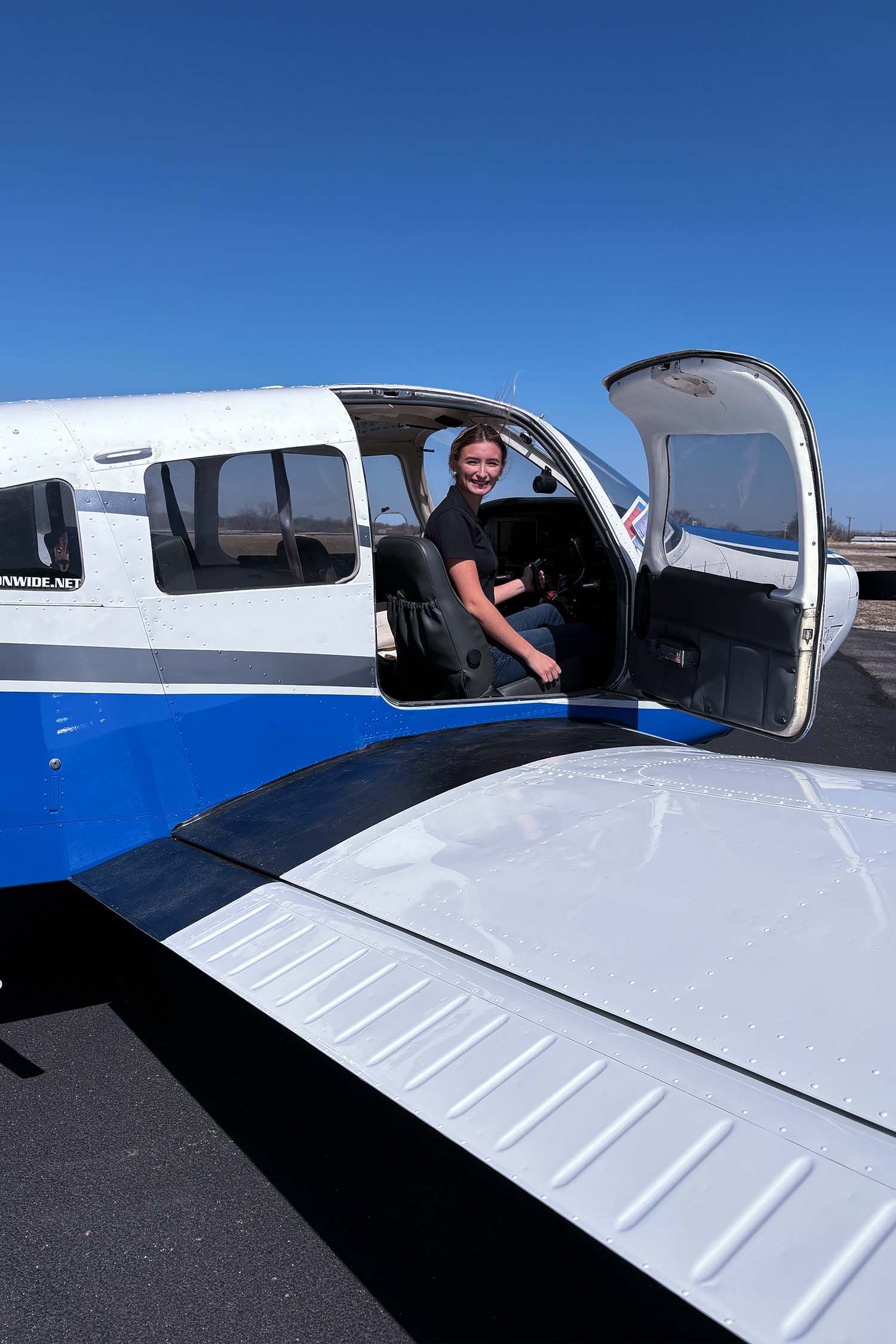 Student standing beside training aircraft with open cabin door.