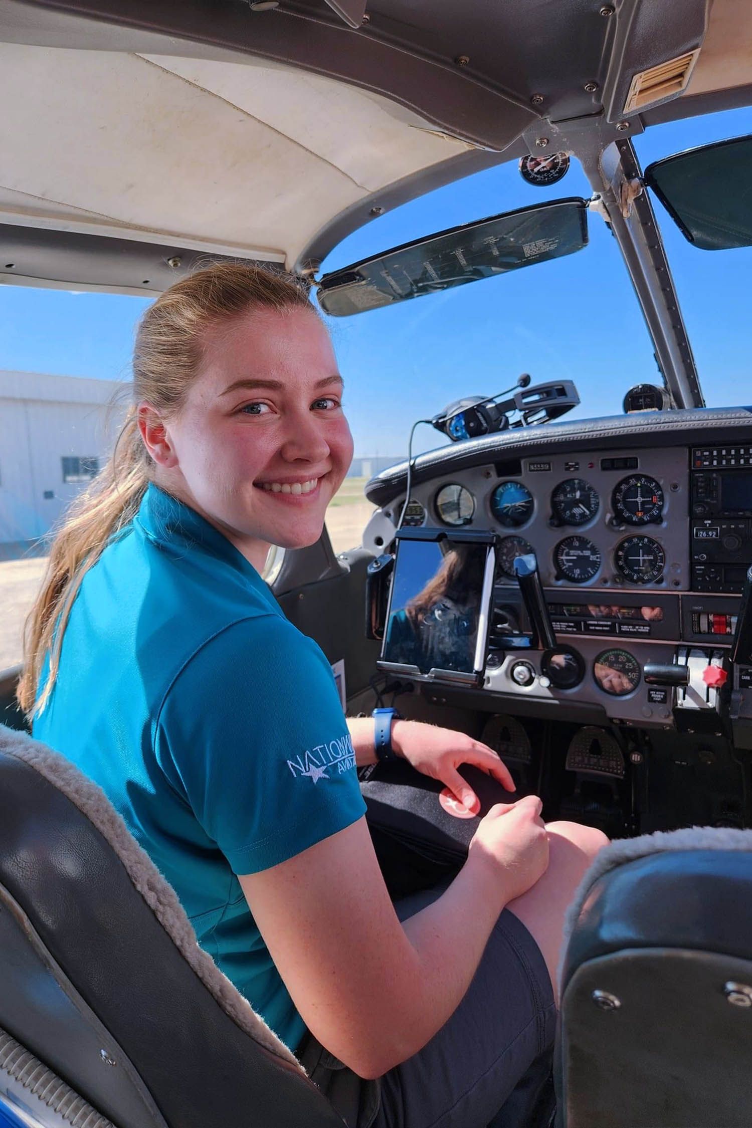 Student pilot smiling inside aircraft with open cabin door on a bright training day.