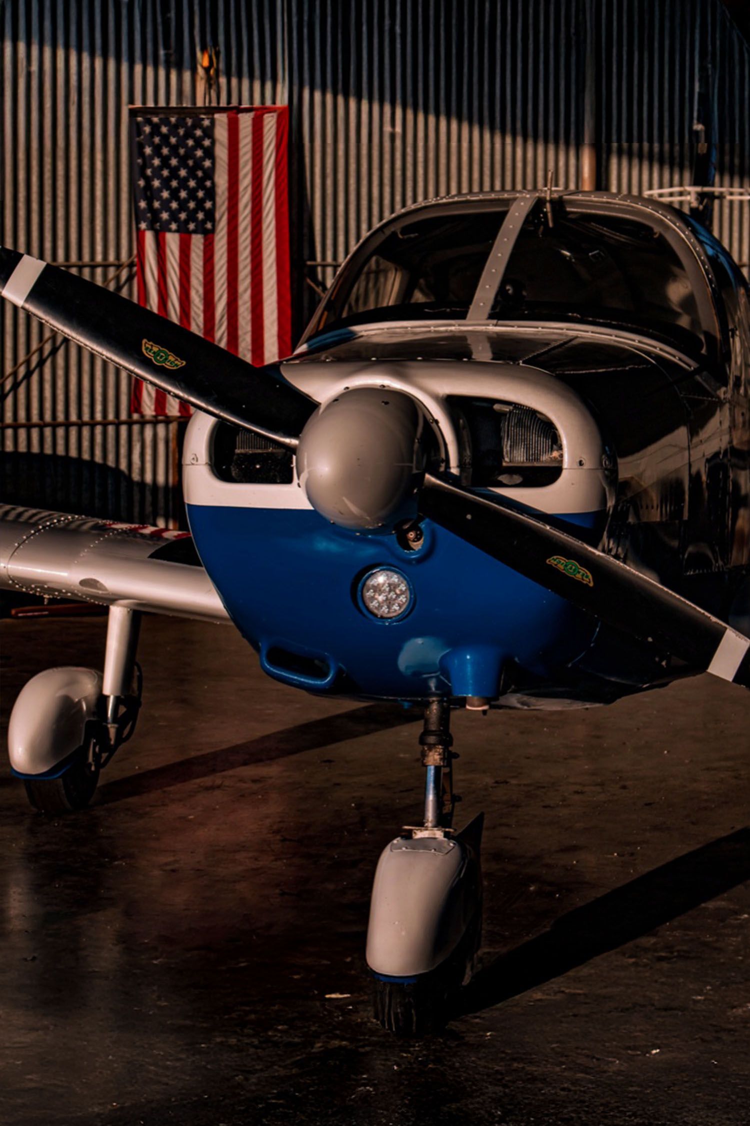 Single-engine aircraft parked in a hangar with an American flag in the background.