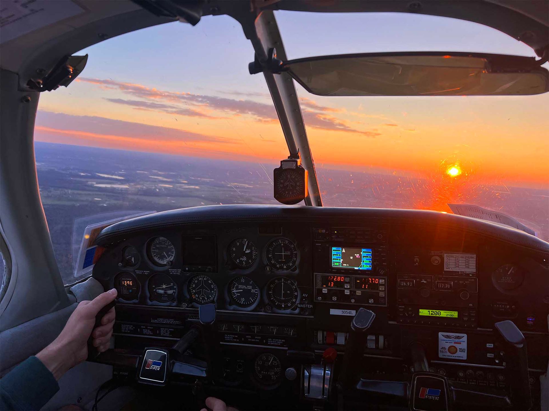 Sunset view from inside a small aircraft cockpit during a training flight.