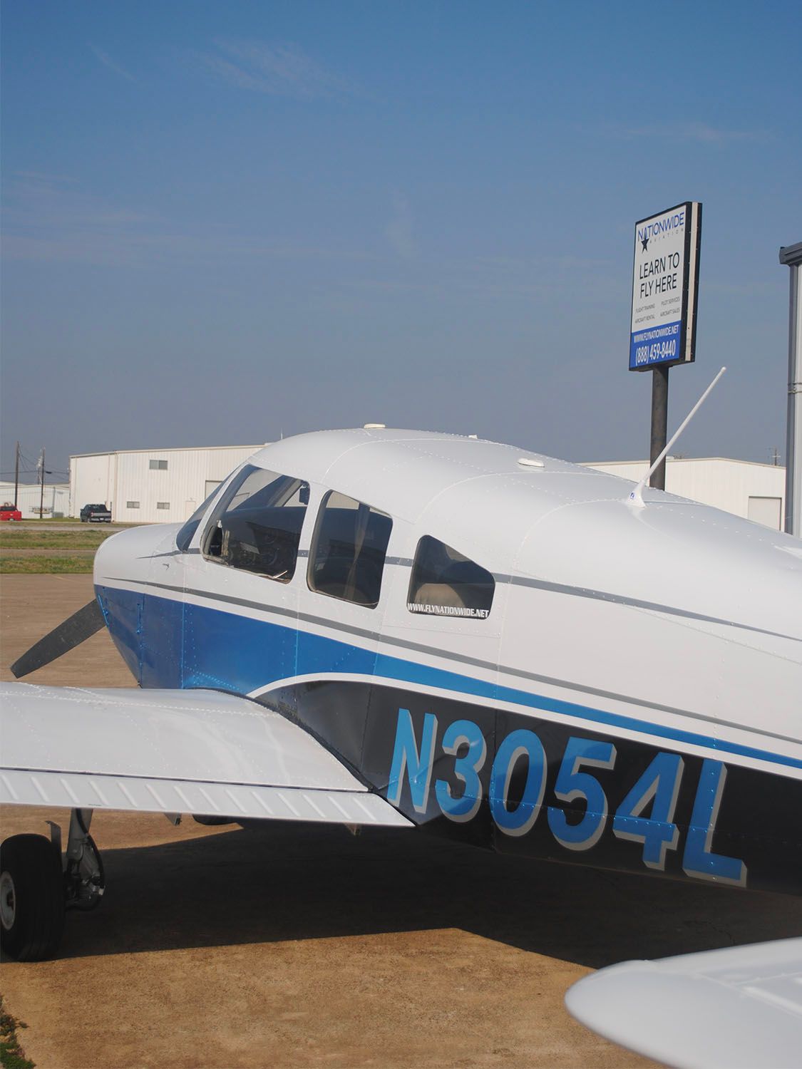 Aircraft wingtip view overlooking an airport sign on a sunny day.