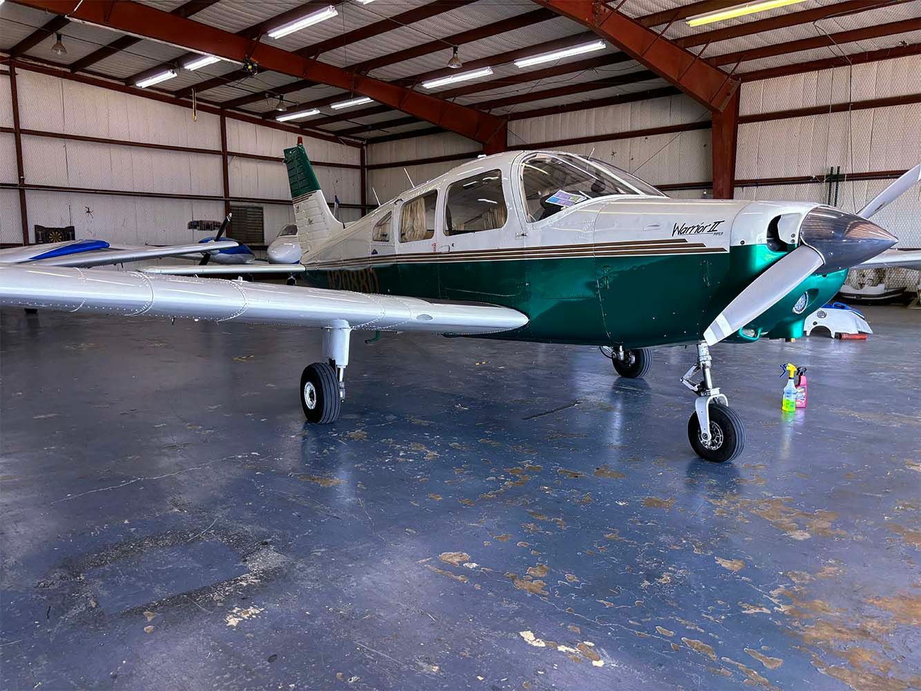 Green and white training aircraft parked inside a spacious hangar.