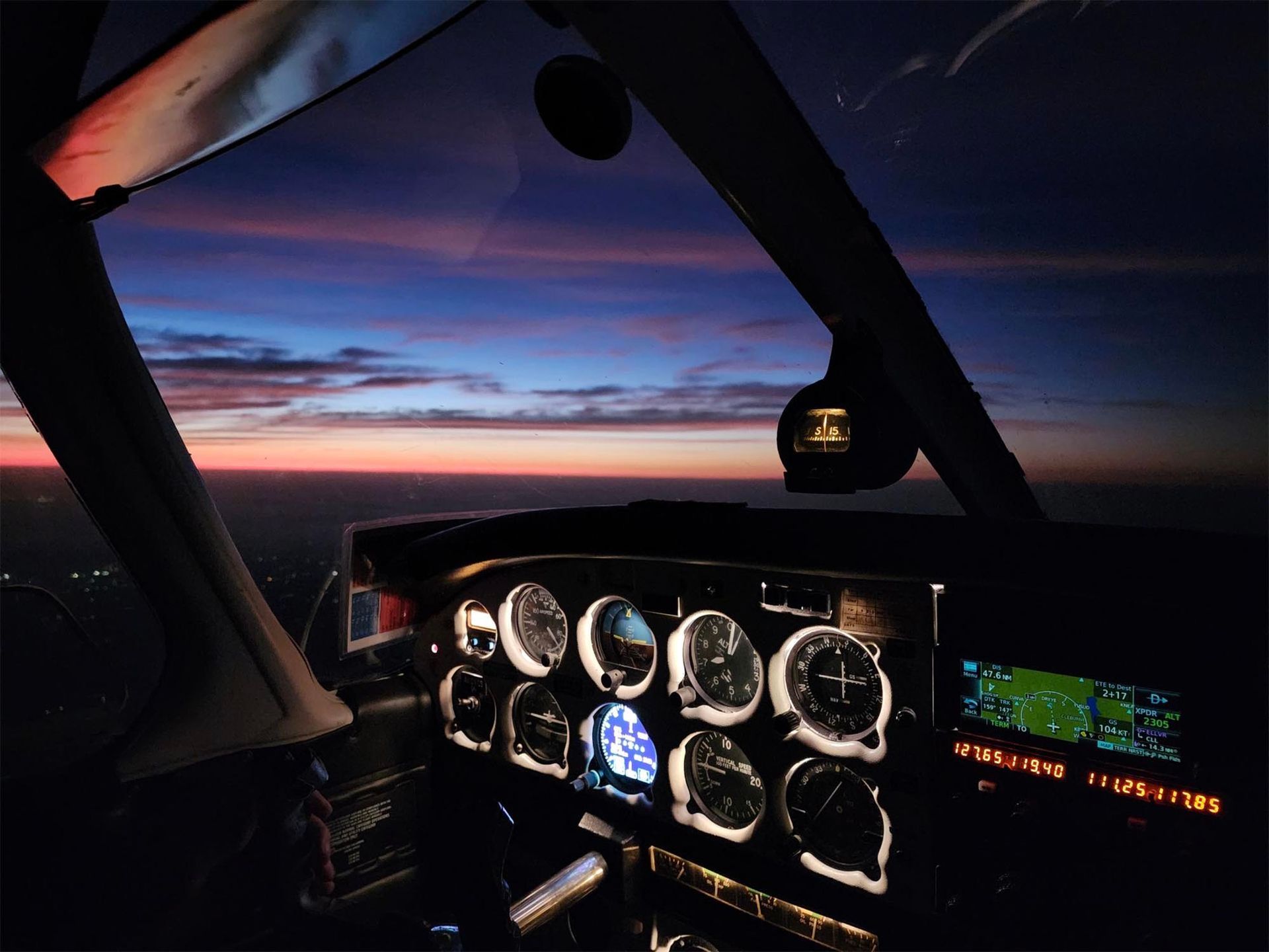 Cockpit view at sunset with flight instruments illuminated.