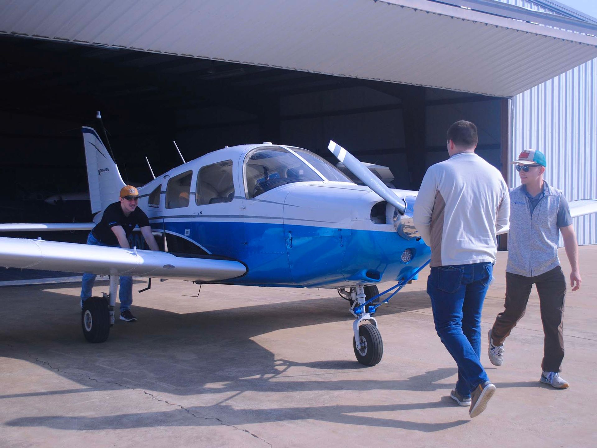 Training aircraft being moved out of the hangar by flight school staff.