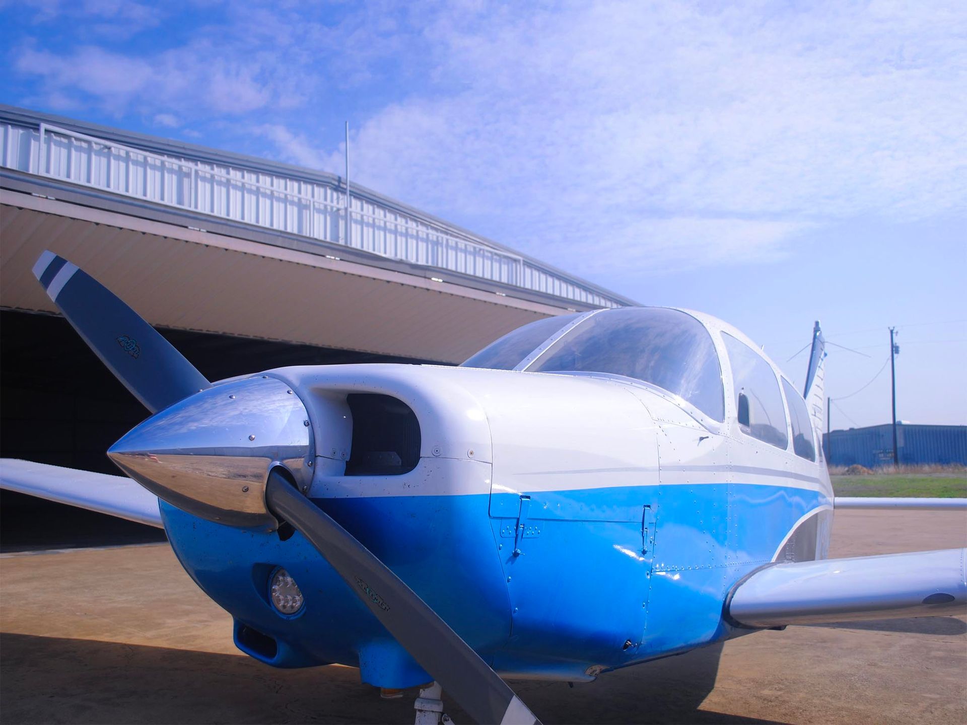 Blue and white aircraft parked near a hangar on a bright day.