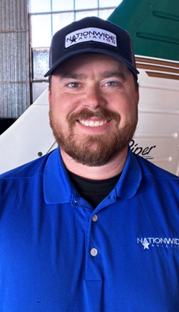Man smiling inside aircraft hangar for aviation school team photo.