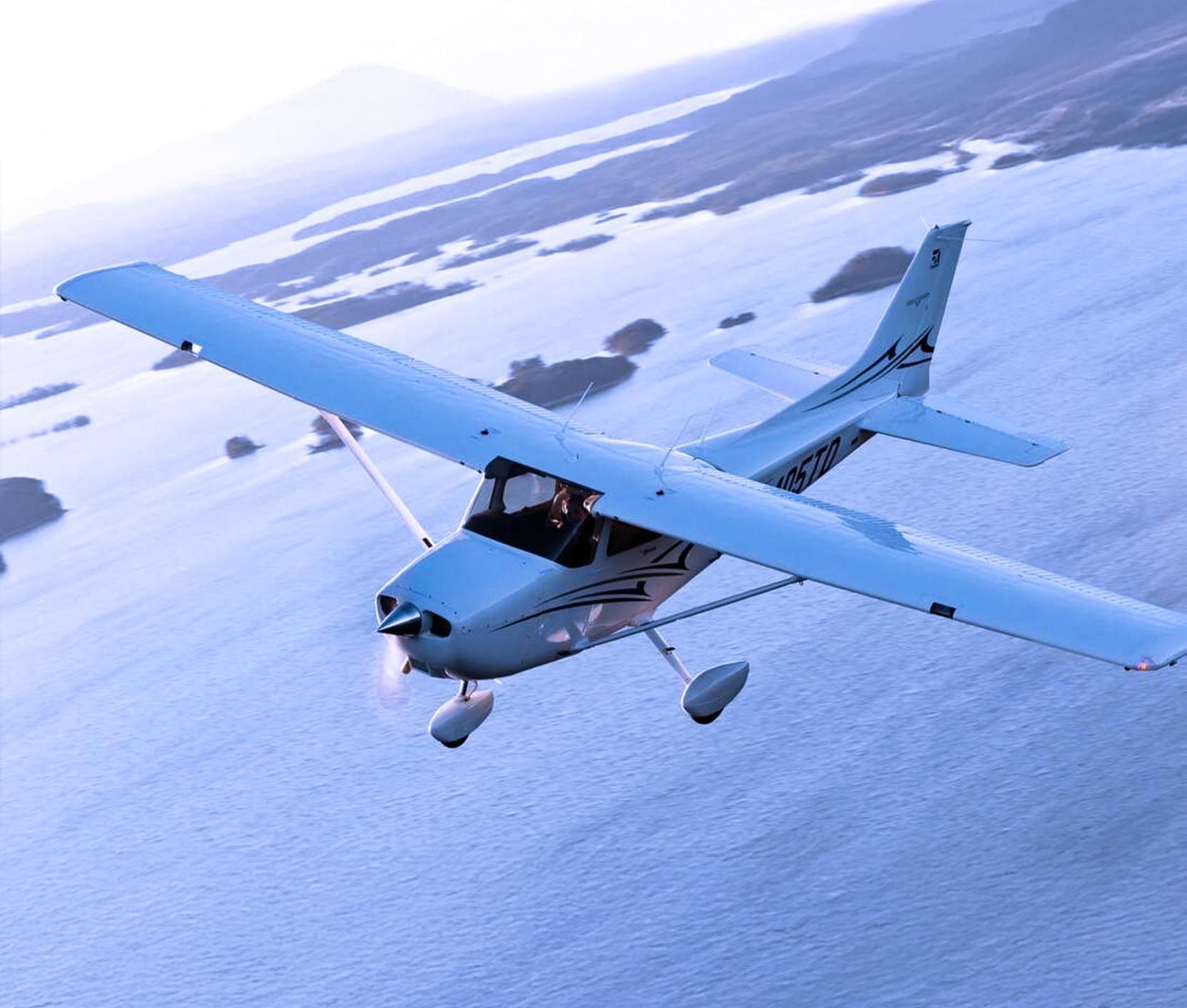 Cessna 172M training aircraft flying over snowy terrain.