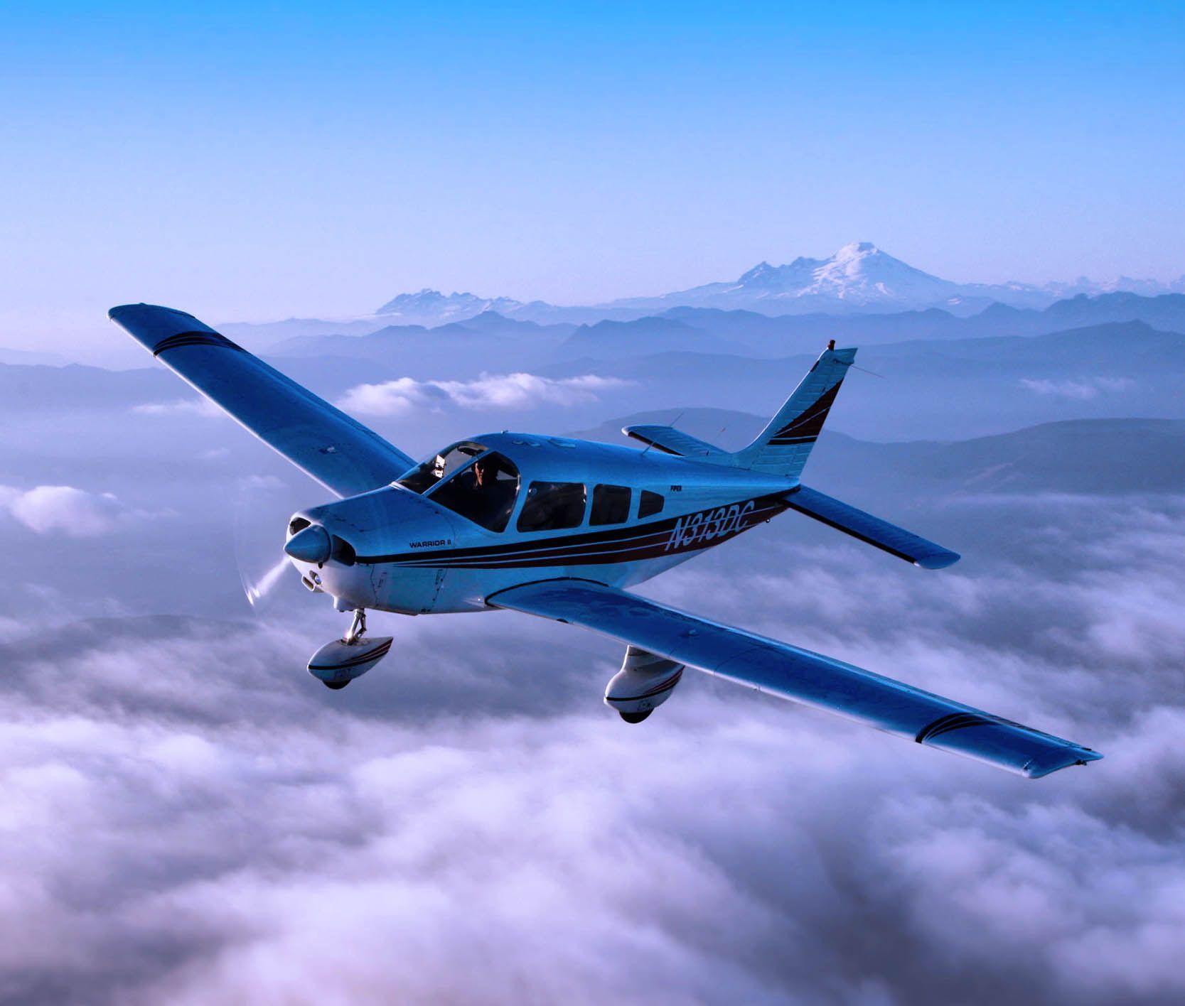 Piper Warrior single-engine aircraft flying with mountains in the distance.