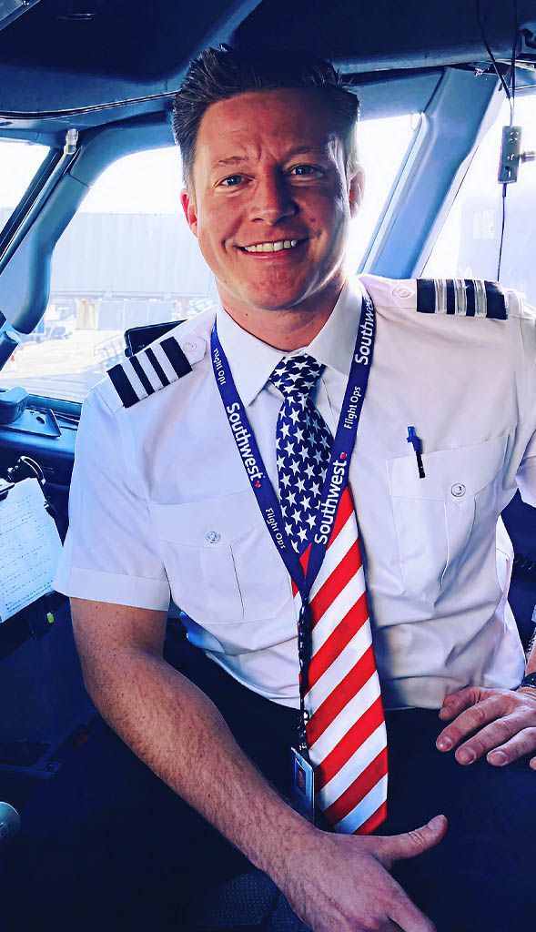 Smiling man seated inside aircraft cockpit for leadership photo.