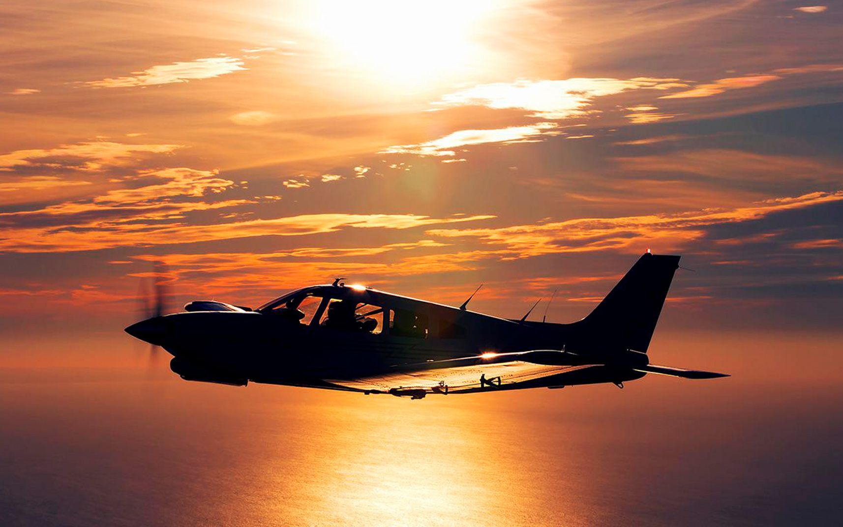 Small aircraft flying at sunset over calm water.