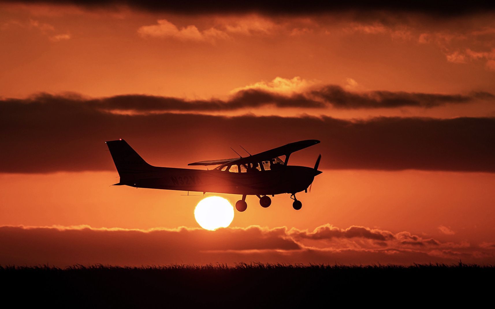 Small aircraft flying at sunset with orange sky in the background.