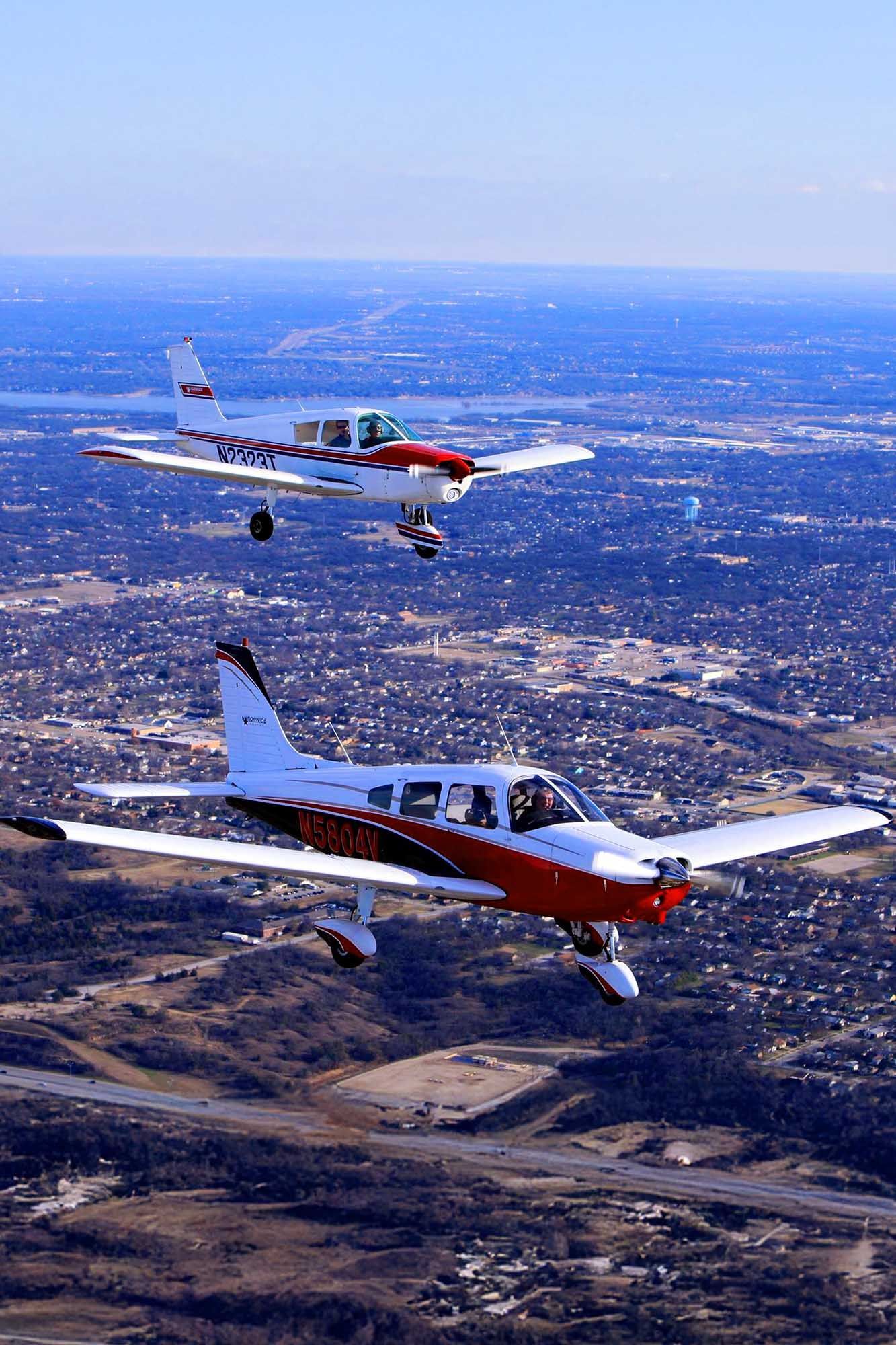 Training aircraft flying over city landscape on a clear day.