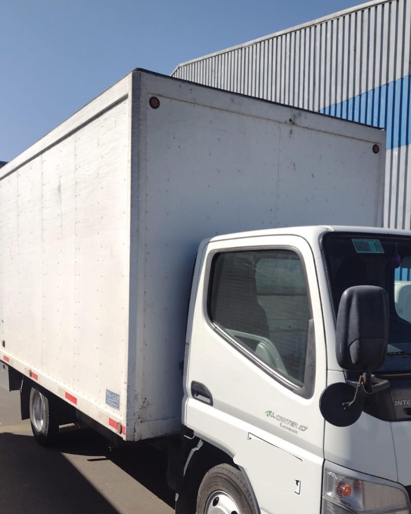 Camión de caja blanca estacionado frente a un edificio de cartón ondulado en un día soleado.