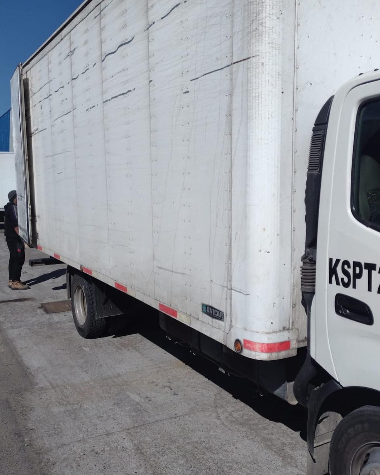 Camión de caja blanca con puerta lateral abierta, persona parada cerca.