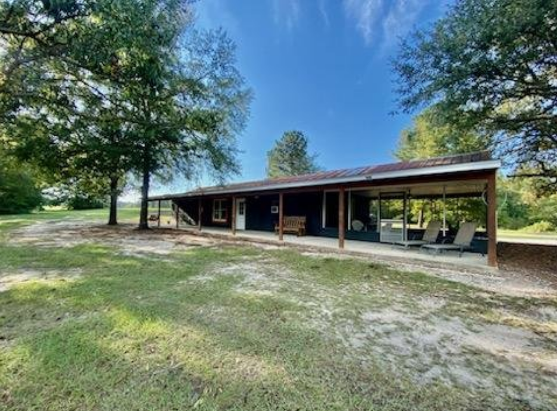 A large house with a porch and trees in the background.