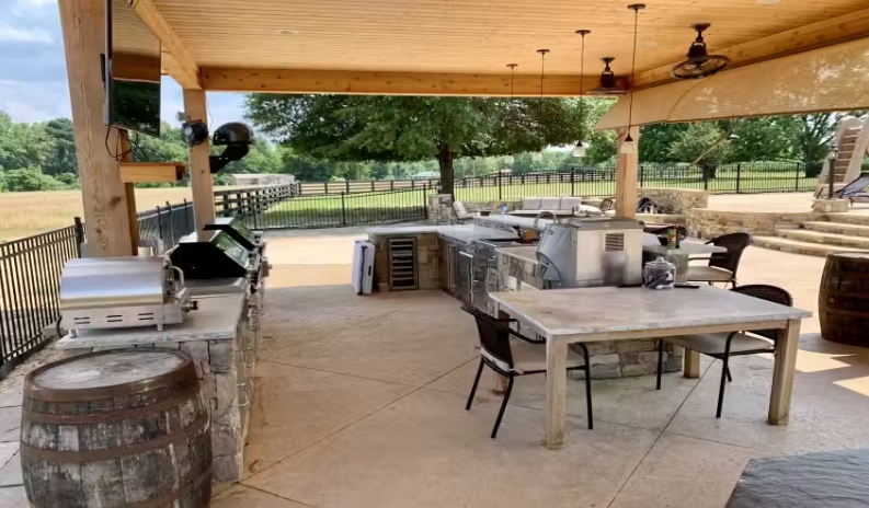 A large outdoor kitchen with a table and chairs and a grill.